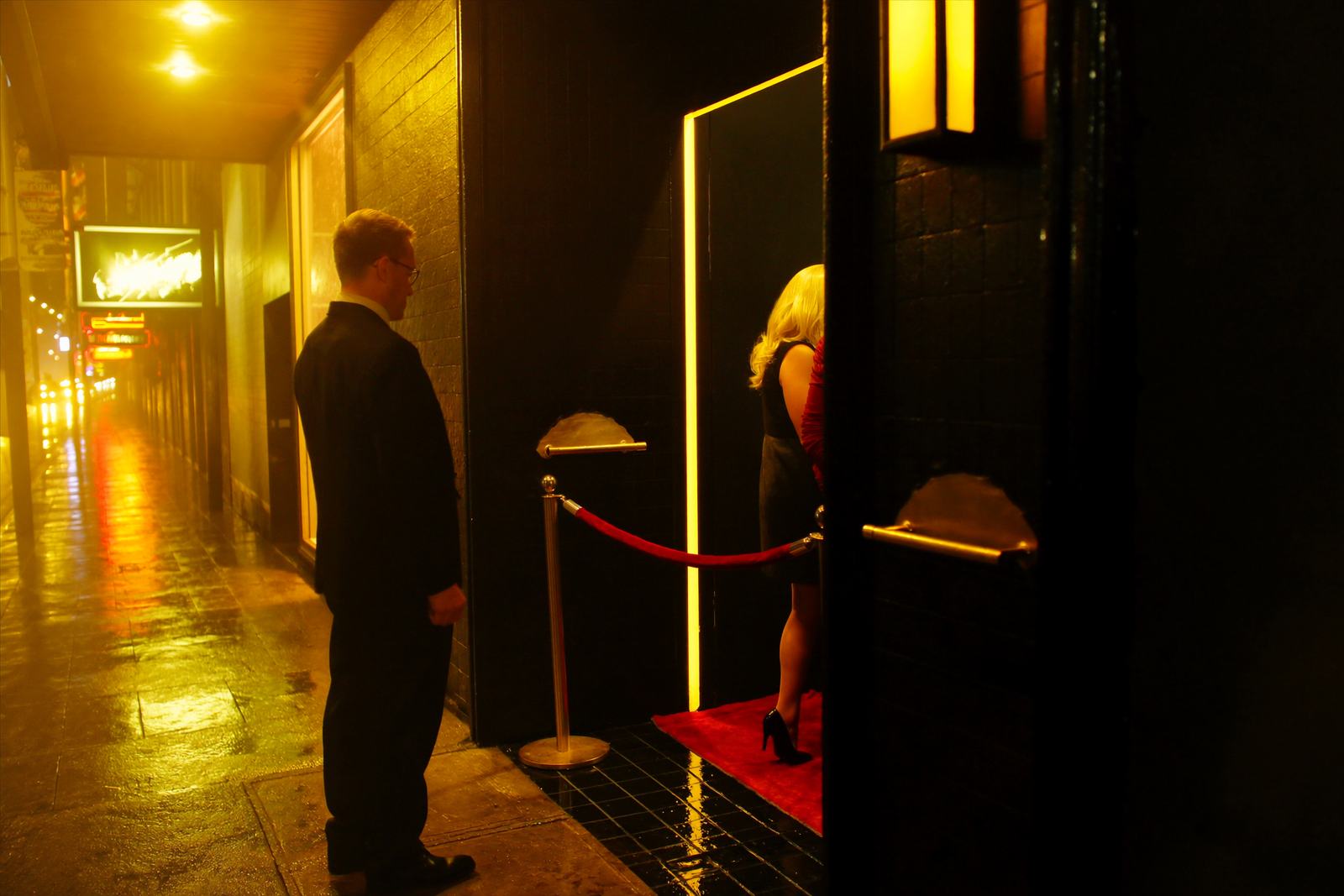 A velvet rope and a red runner at a lit doorway at night